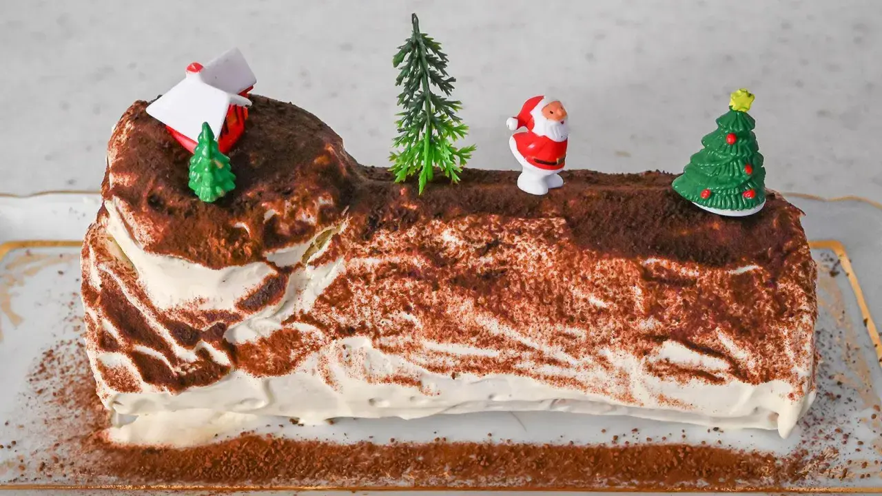 Eine festliche bûche de noël deutsch, verziert mit Weihnachtsmann, Bäumen und einem Haus.