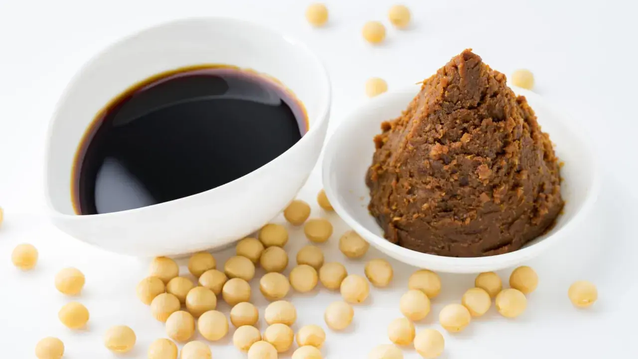 Miso-Paste und Sojasauce in weißen Schalen, umgeben von Sojabohnen. Eine köstliche Alternative zu Hefeflocken für herzhafte Gerichte.