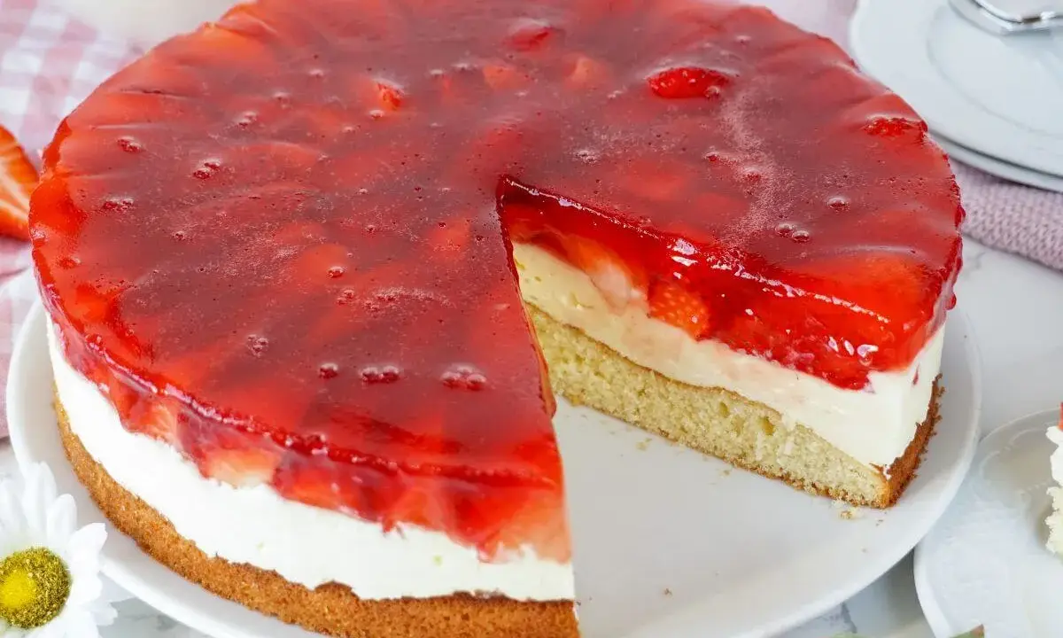 Ein saftiger erdbeerkuchen mit vanillepudding und einer glänzenden Erdbeer-Gelee-Schicht. Ein Stück ist bereits herausgeschnitten.