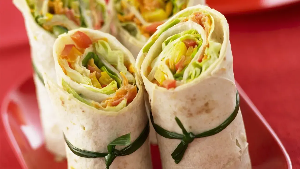 Vier gesunde wraps gefüllt mit knackigem Salat, Paprika und Karotten, kunstvoll mit grünen Bändern zusammengebunden.
