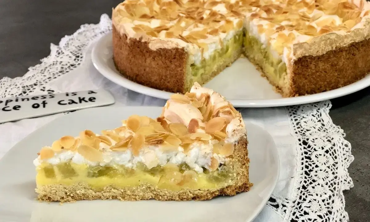 Ein köstlicher Rhabarberkuchen mit Pudding und Baiser, bestreut mit Mandelblättchen. Ein Stück Glück auf einem Teller.