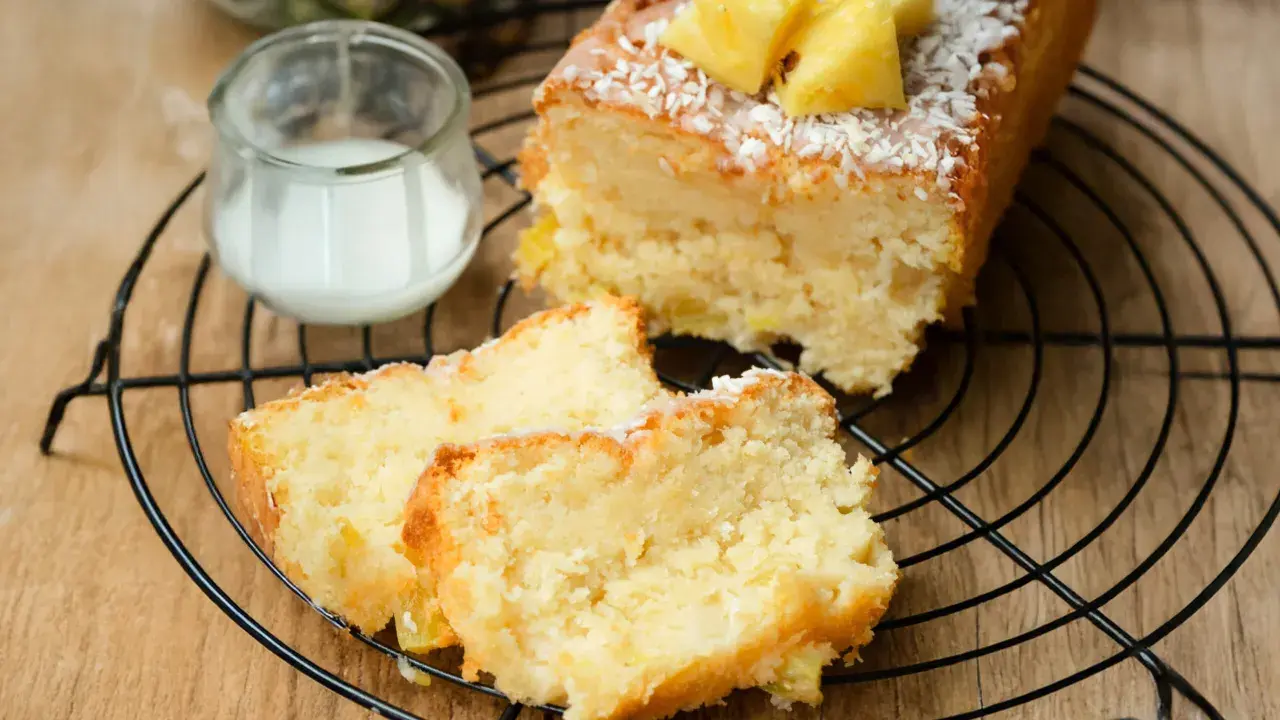 Saftiger ananas kokos kuchen mit frischer Ananas und Kokosraspeln, serviert auf einem Gitter mit einem Glas Milch.