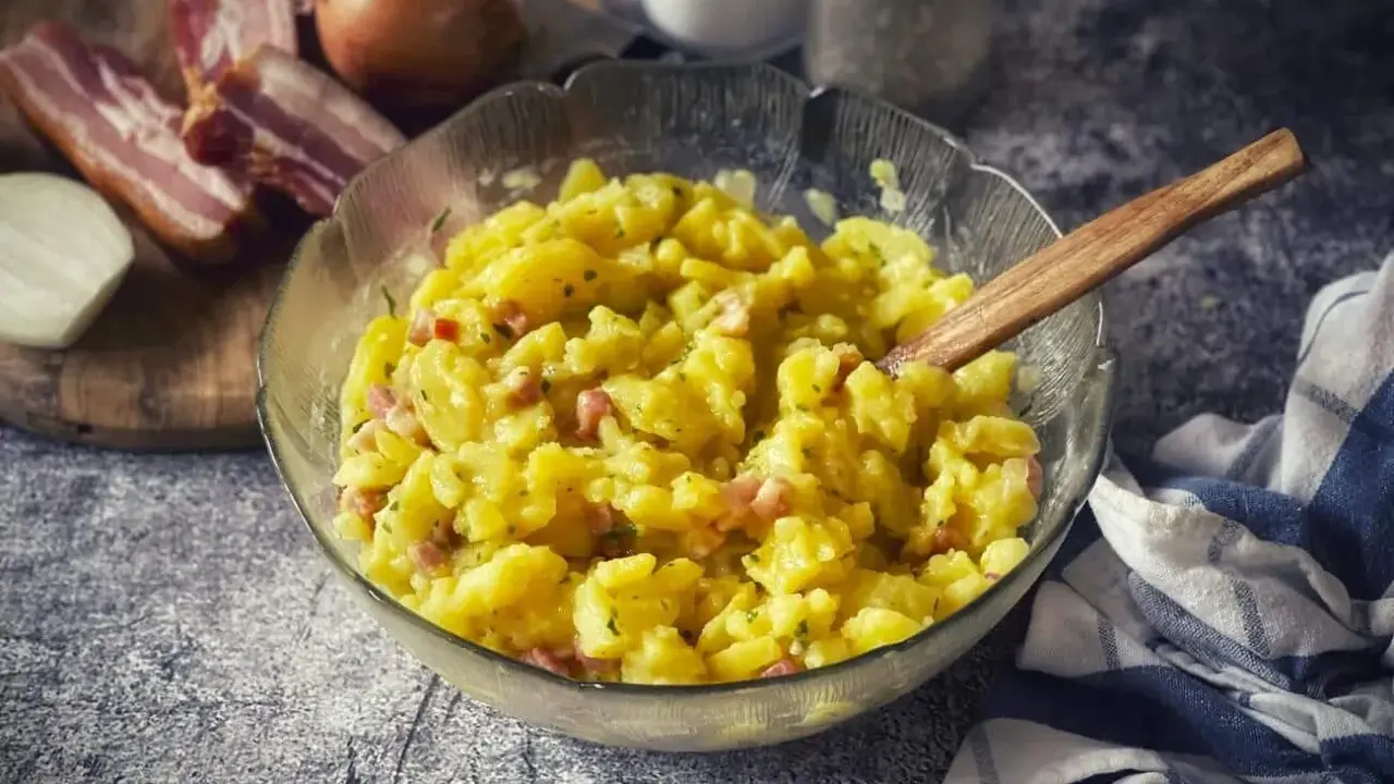 Schüssel mit warmem Kartoffelsalat, garniert mit Speck und Zwiebeln, bereit zum Servieren.