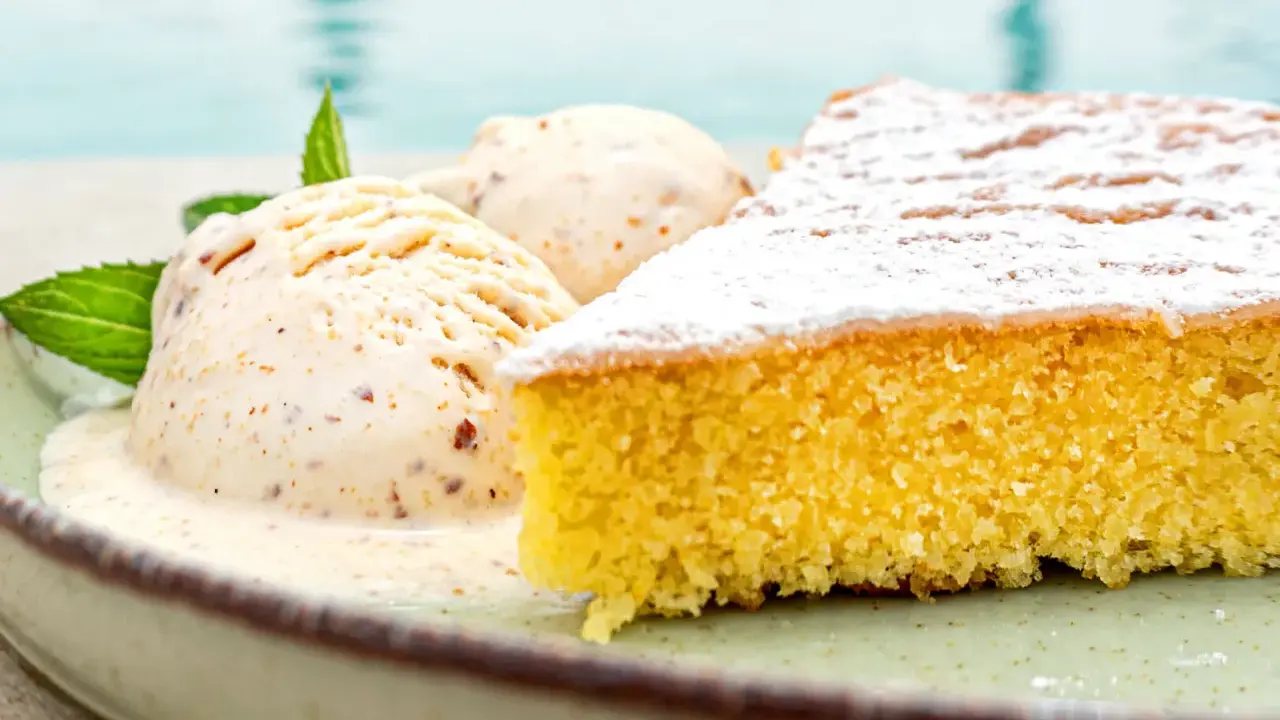 Ein Stück mallorquinischer Mandelkuchen mit zwei Kugeln Eis und Minze, serviert auf einem Teller am Pool.