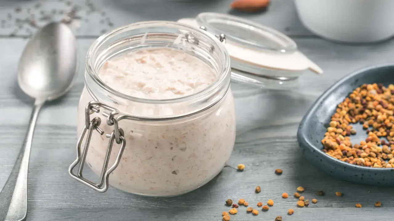 Ein Glas cremiger Haferflocken-Pudding steht bereit, daneben eine Schale mit Pollen und ein Löffel.