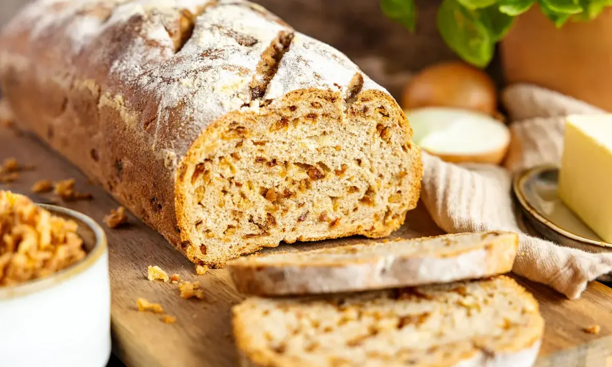 Frisch gebackenes Zwiebelbrot mit knusprigen Röstzwiebeln, bereit für ein köstliches Zwiebelbrot Rezept. Daneben Butter und frische Kräuter.