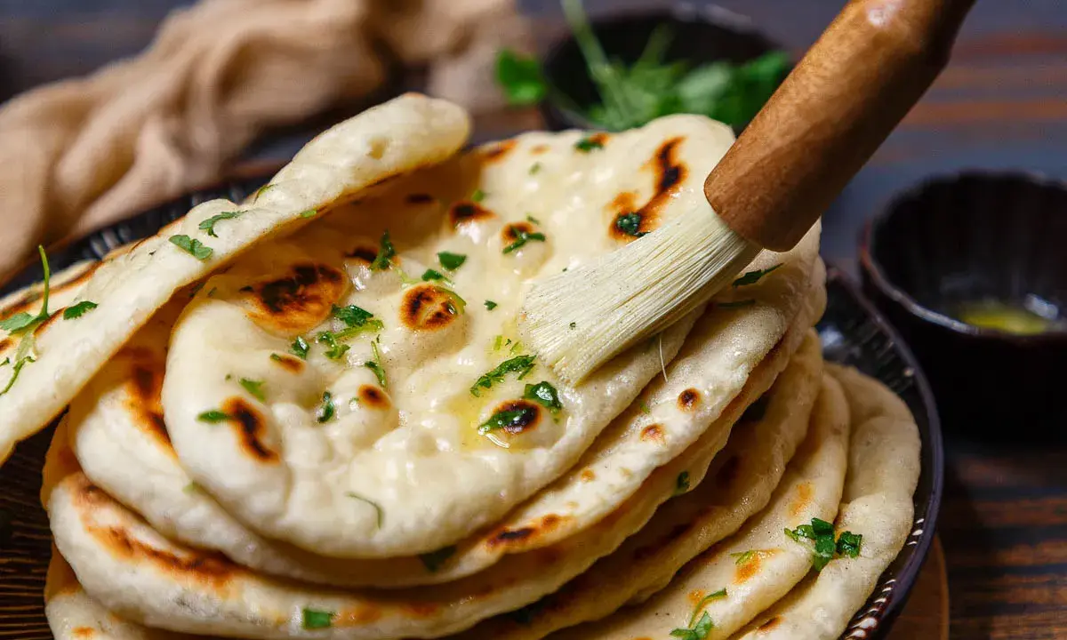 Frisch gebackenes Naan Brot wird mit Butter bestrichen und mit Kräutern bestreut.