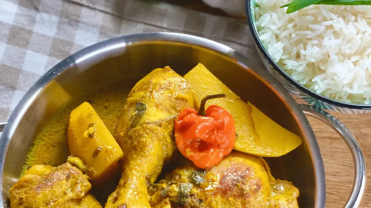 Colombo de poulet mit Kartoffeln und einer scharfen Chili, daneben eine Schüssel Reis.