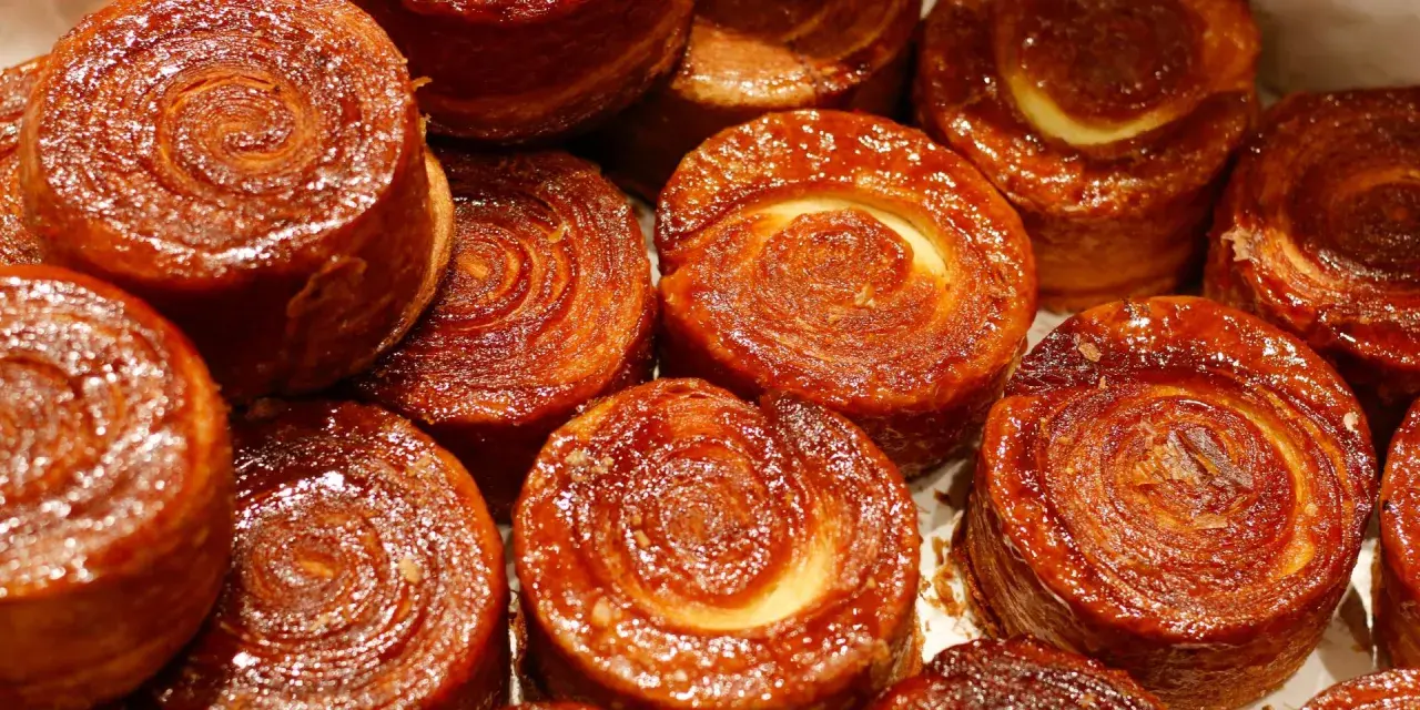 Nahaufnahme von karamellisierten Kouign Amann Gebäckstücken mit spiralförmiger Teigstruktur.