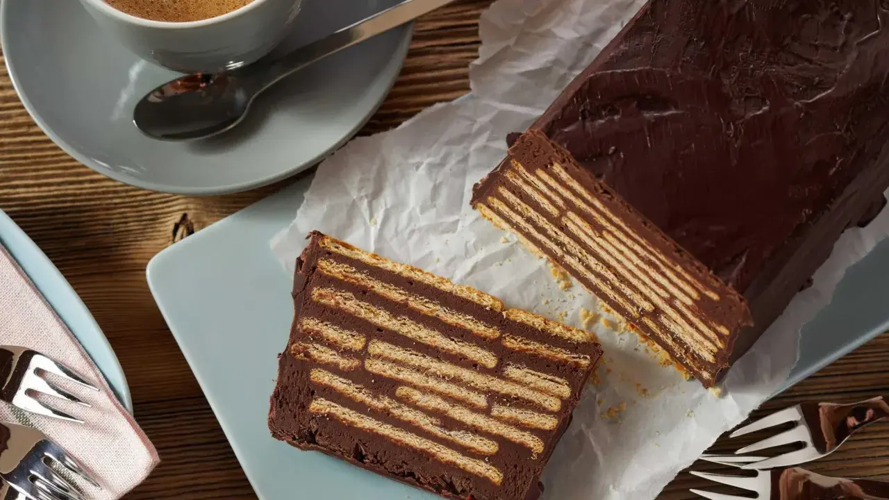 Ein Stück Schokoladenkuchen, der wie ein kalter Hund aussieht, mit Keksen und Schokoladencreme geschichtet. Daneben eine Tasse Kaffee.