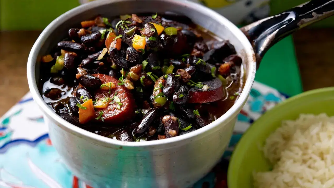 Herzhaftes schwarze bohnen rezept im Topf, mit Wurst und Gemüse, daneben eine Schüssel Reis.