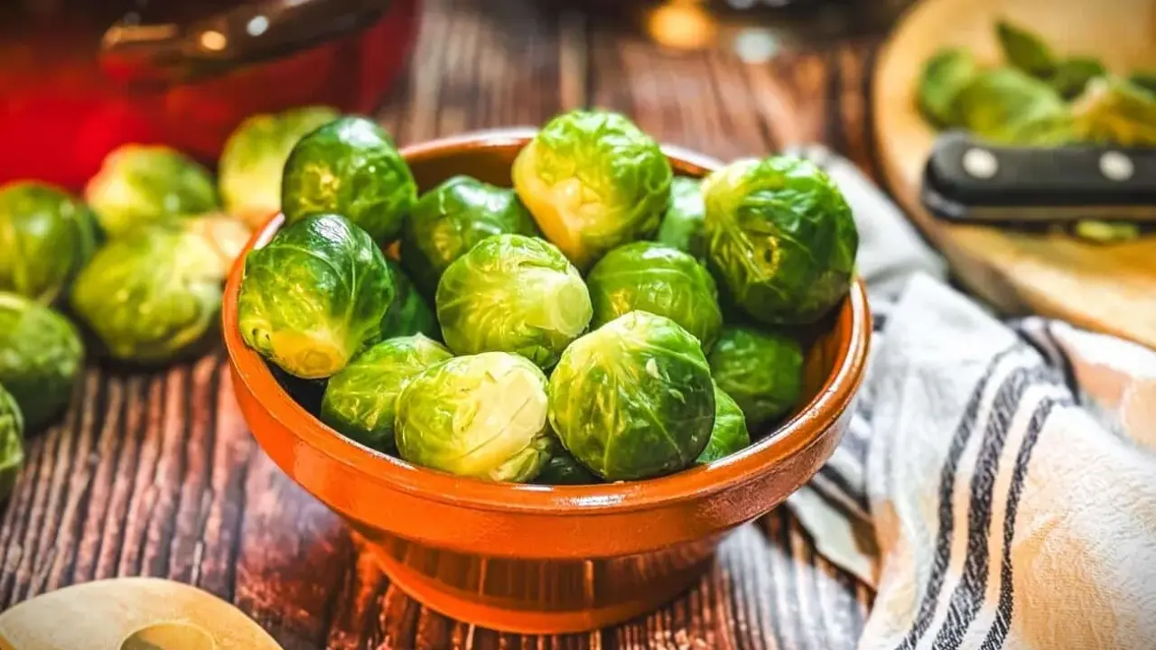 Frischer Rosenkohl in einer Schale, bereit, rosenkohl zuzubereiten wie Oma. Ein Holzlöffel liegt daneben.