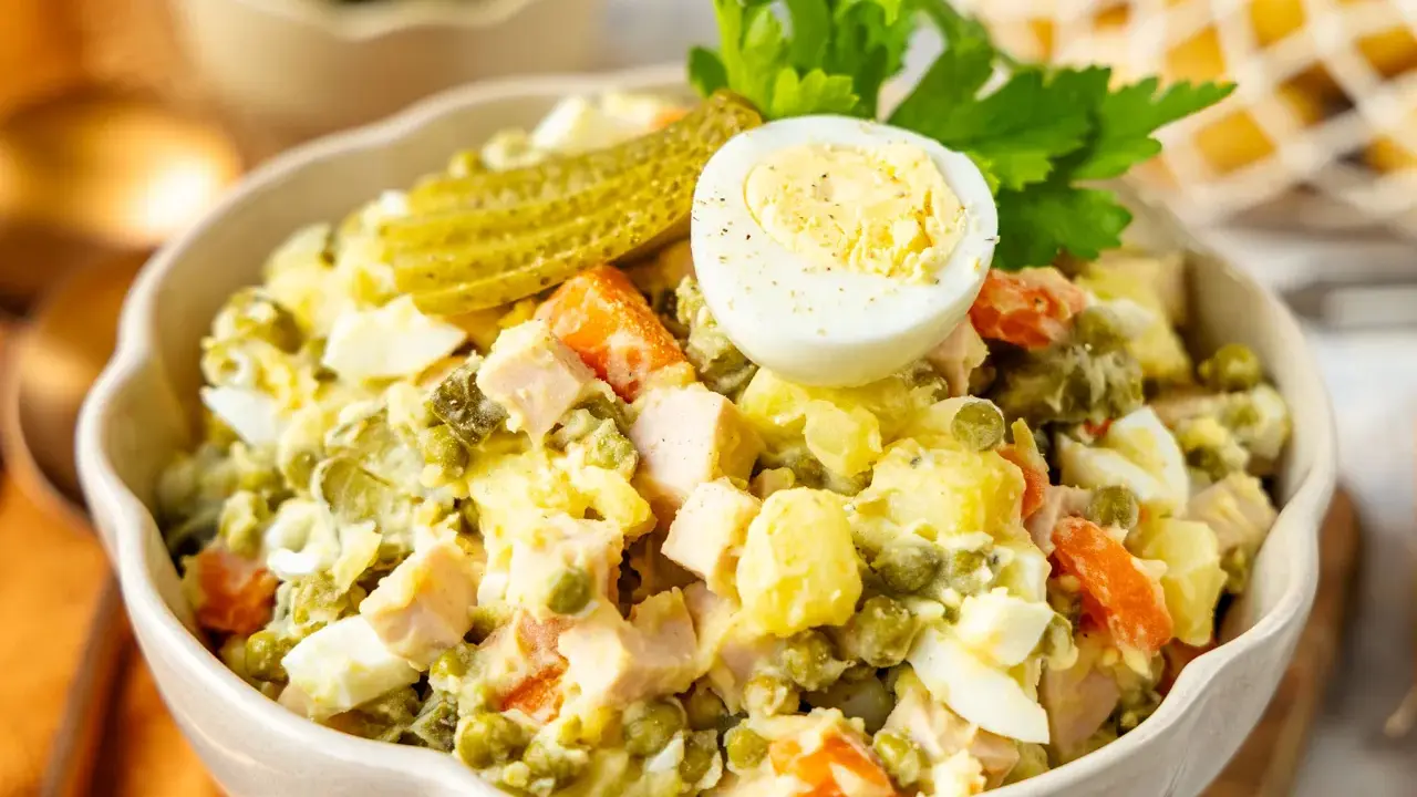 Ein cremiger Olivier Salat mit Erbsen, Karotten, Eiern und Gewürzgurken, garniert mit einer halben Eierschale und Petersilie.