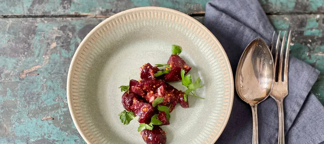 Ein köstlicher Rote Bete Feta Salat mit frischer Petersilie, serviert auf einem rustikalen Teller. Daneben liegen Löffel und Gabel.