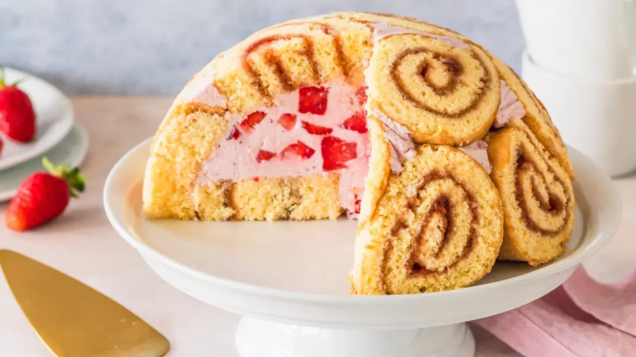 Halbierte Erdbeer Charlotte auf einer Tortenplatte, gefüllt mit Erdbeercreme und frischen Erdbeeren, umhüllt von Biskuitrollen.