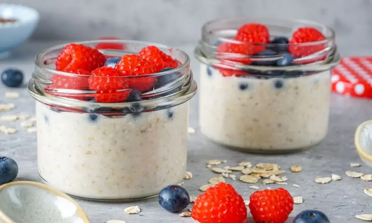 Zwei Gläser mit Overnight Oats, garniert mit frischen Himbeeren und Blaubeeren. Perfekt für ein leckeres, low carb Frühstück.