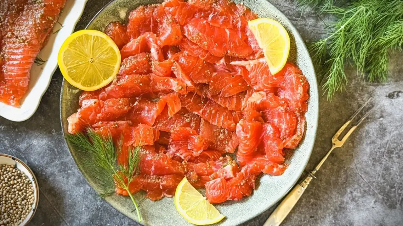 Frisch gebeizter Lachs auf einem Teller, garniert mit Zitronenscheiben und Dill. Daneben eine Schale mit Koriandersamen.