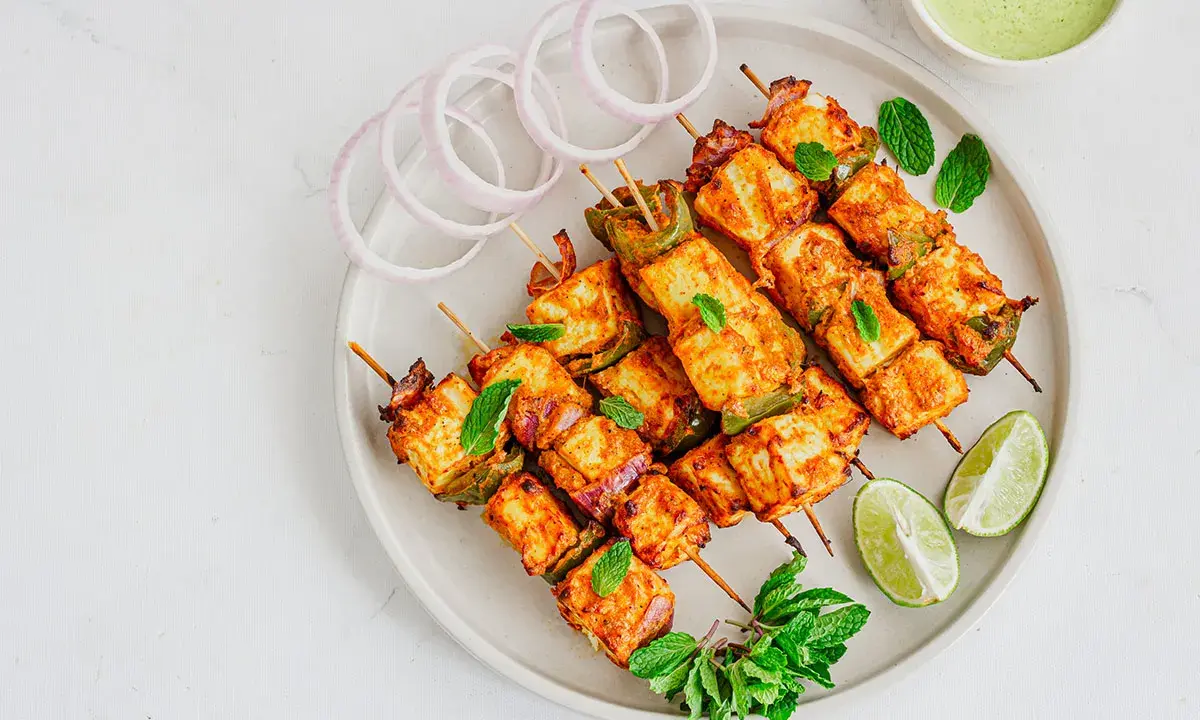 Saftiges paneer tikka auf Spießen, garniert mit Minze, Zwiebelringen und Limettenspalten.