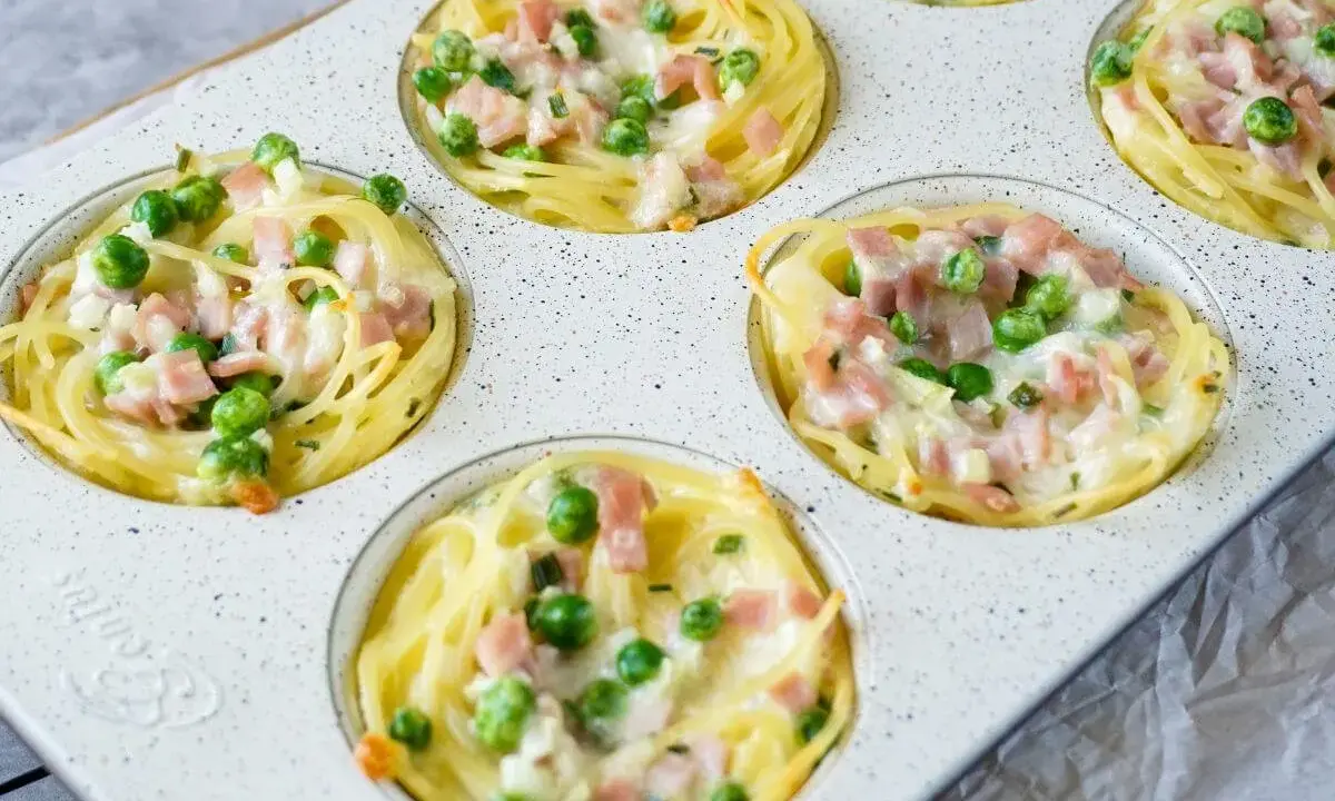 Köstliche Muffins aus nudeln vom vortag, gefüllt mit Erbsen und Schinken, überbacken mit Käse.
