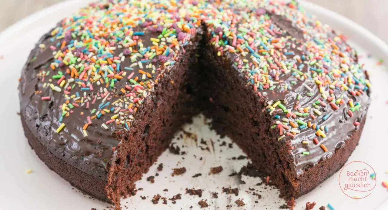 Schokoladenkuchen ohne Mehl und Ei, mit glänzender Glasur und bunten Streuseln. Ein Stück fehlt, was Lust auf mehr macht.