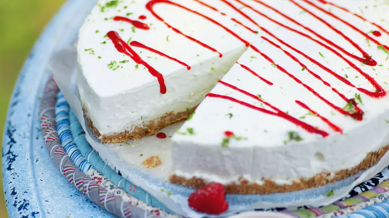 Cremiger Kuchen ohne Backen, dekoriert mit rotem Sirup und Limettenabrieb. Ein Stück ist bereits angeschnitten.