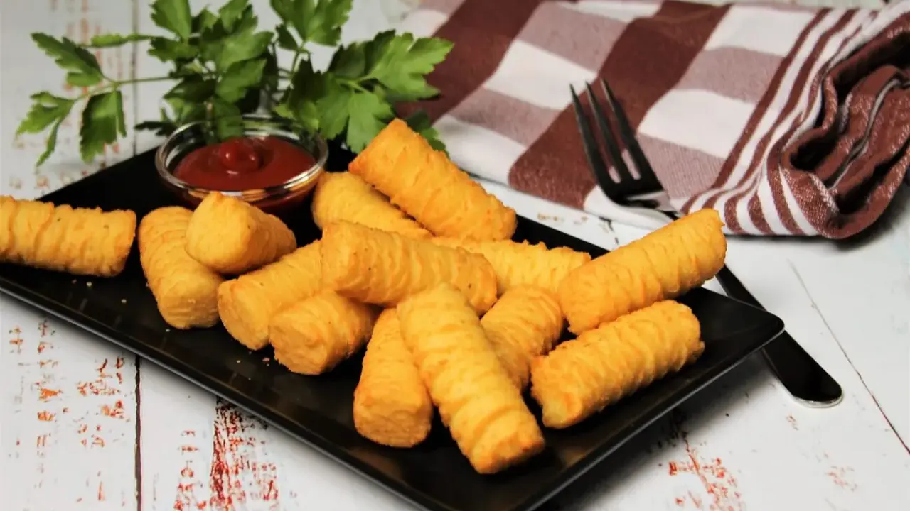 Goldbraune Kroketten, frisch zubereitet, liegen auf einem schwarzen Teller. Dazu gibt es Ketchup und frische Petersilie. Perfekt zum selber machen!