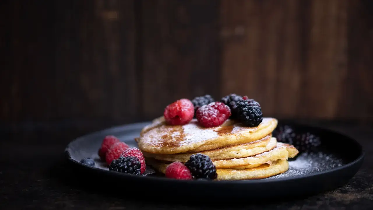 Ein Stapel fluffiger Pancakes, garniert mit frischen Beeren und Puderzucker. Ein perfektes pancakes rezept fluffig für jeden Anlass.