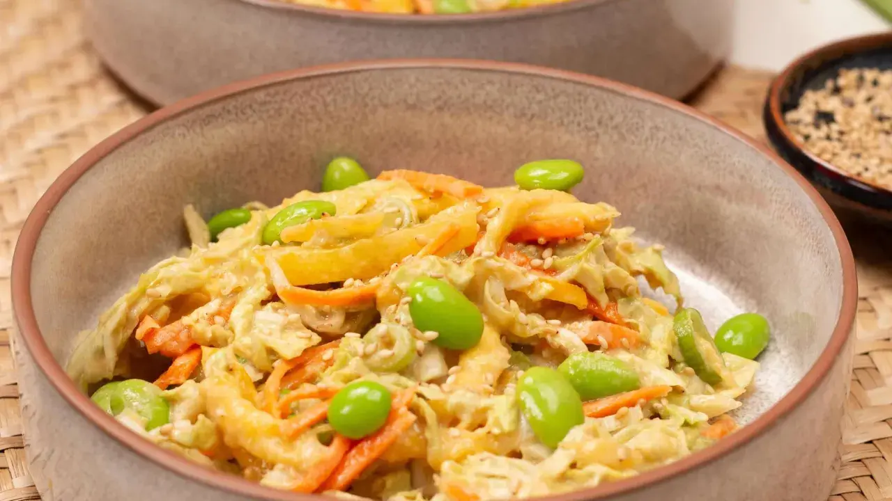 Ein cremiger asiatischer Salat mit knackigem Kohl, Karottenstreifen und Edamame, garniert mit Sesam.