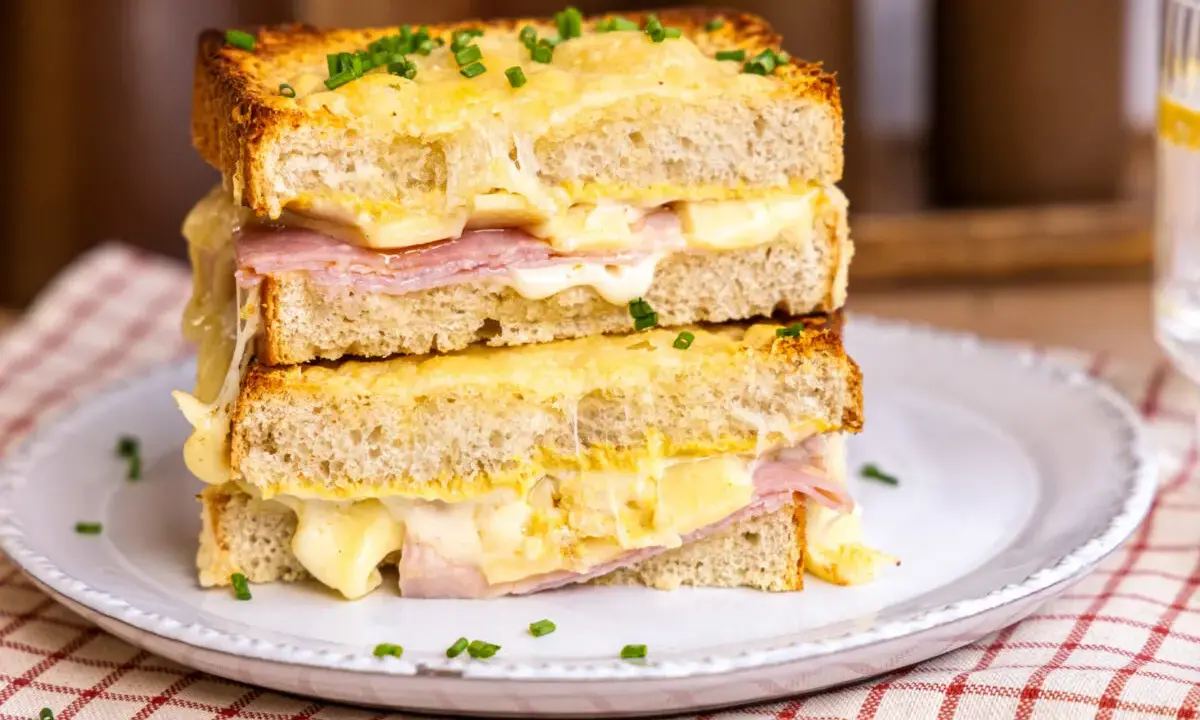 Ein gestapelter Croque Monsieur mit geschmolzenem Käse, Schinken und Schnittlauch auf einem Teller.