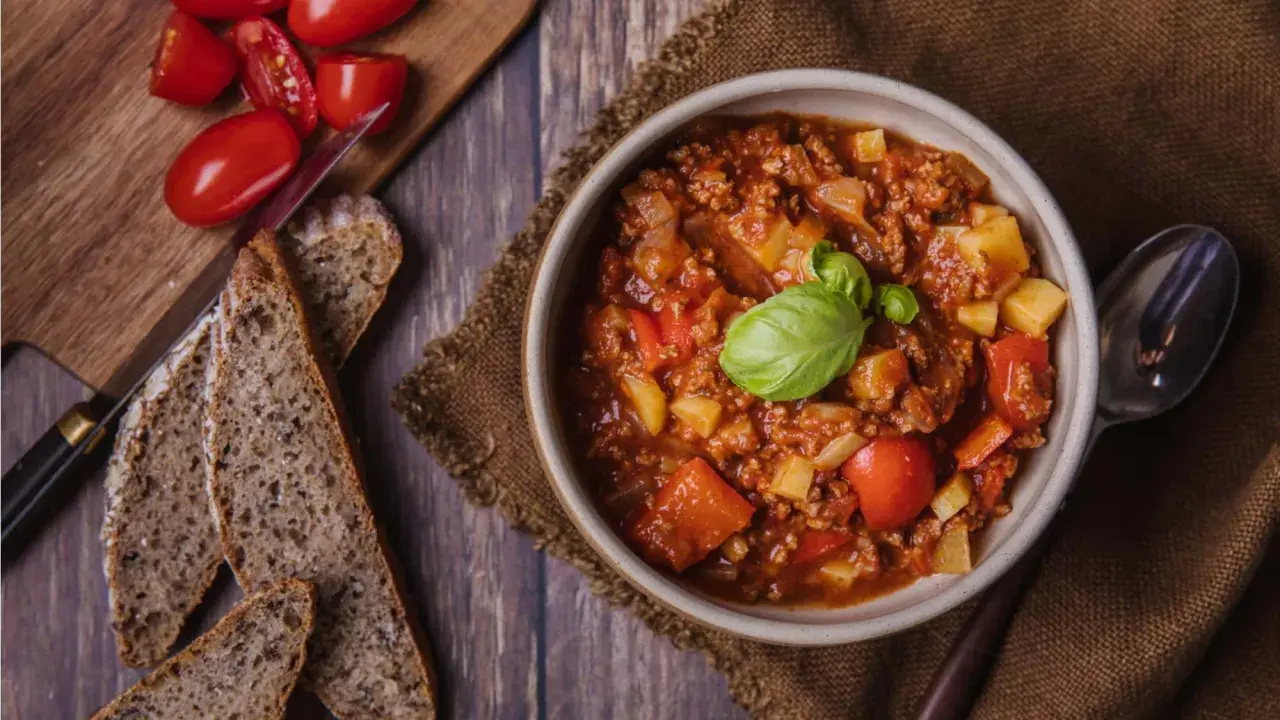 Herzhaftes Bauerntopf Rezept: Hackfleisch, Kartoffeln und Tomaten in einer Schüssel, garniert mit Basilikum. Dazu gibt es rustikales Brot.