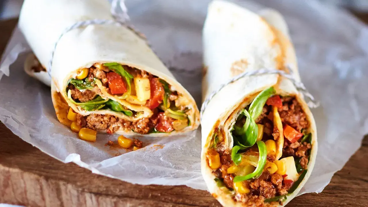 Zwei leckere wraps mit hackfleisch, Mais, Tomaten und Salat, serviert auf Backpapier.