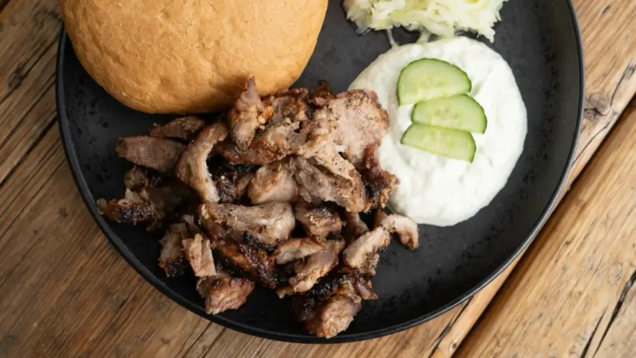 Ein Teller mit gegrilltem Fleisch, Tzatziki, Gurkenscheiben, Krautsalat und einem Brötchen – perfekt für ein leckeres Gyros Rezept.
