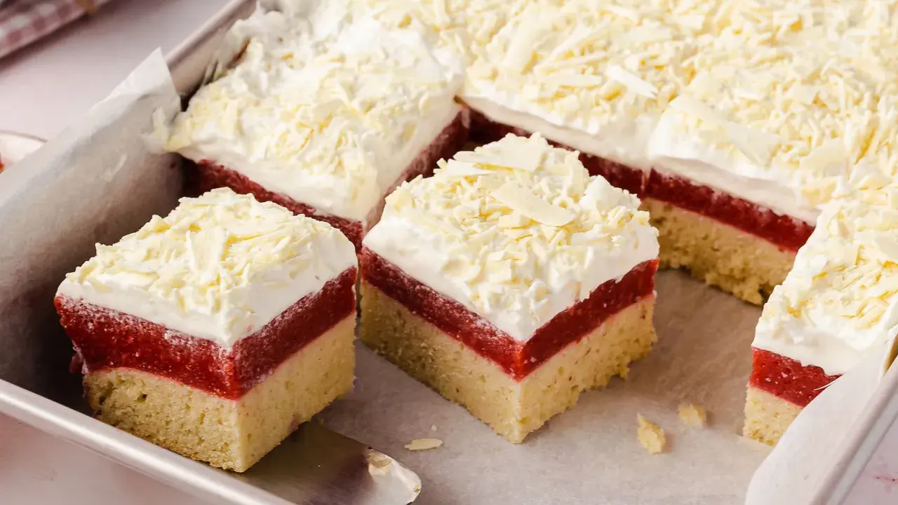 Schneeweiße Sahne und rote Fruchtschicht auf hellem Boden, bestreut mit weißer Schokolade. Ein köstlicher Frau Holle Kuchen, der zum Reinbeißen einlädt.