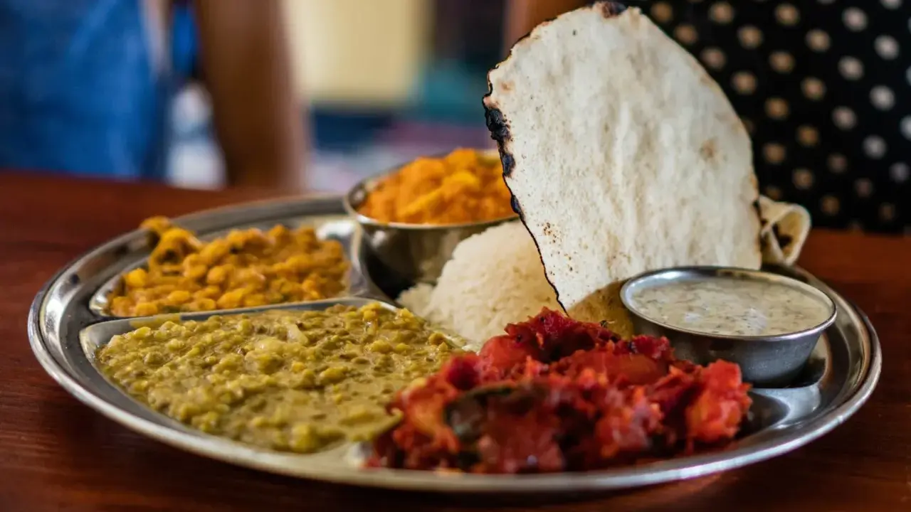 Vielfalt an indischen Gerichten auf einer Thali-Platte: Reis, Linsen, Curry und Papadum.