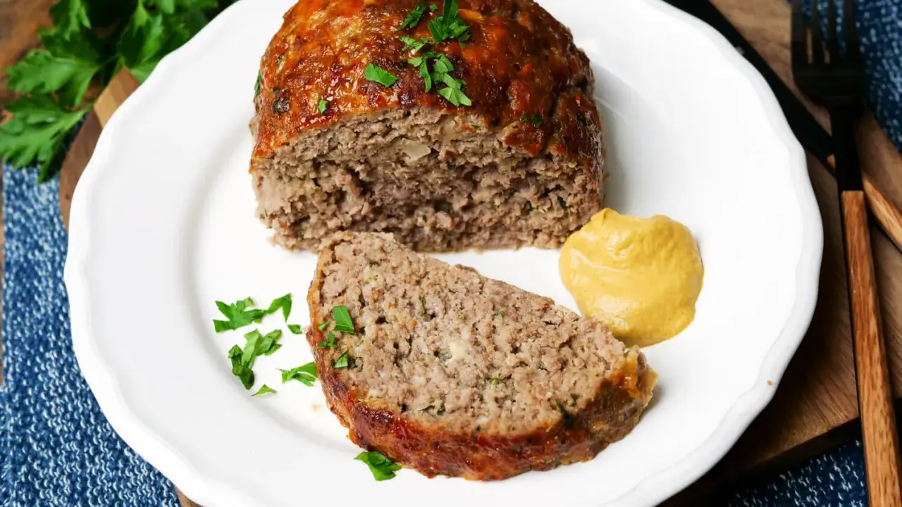 Saftiger hackbraten im ofen, auf einem Teller mit Senf und Petersilie garniert.