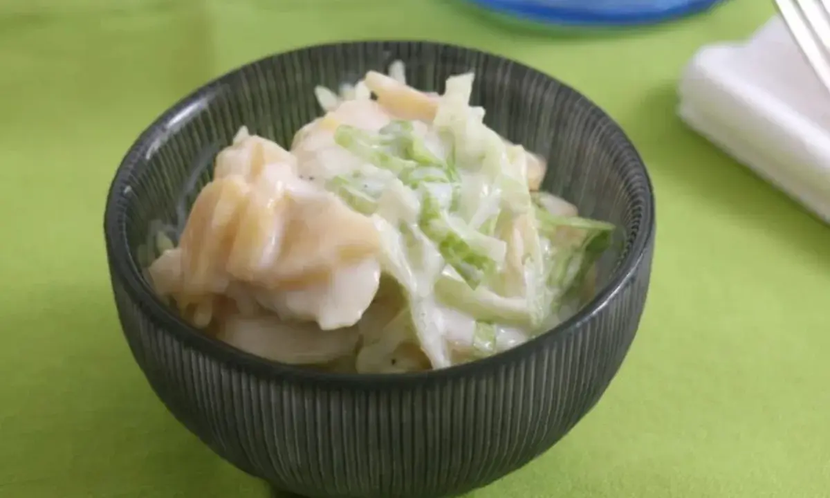 Ein cremiger Kartoffelsalat mit Joghurt und knackigem Gemüse, serviert in einer dunklen Schüssel auf einem hellgrünen Tischtuch.