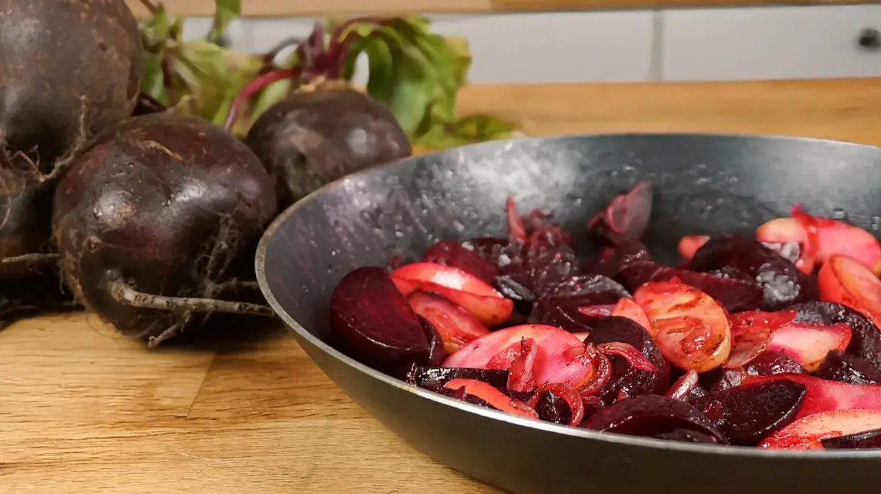 Rote Bete wird in einer Pfanne zubereitet, ein köstliches Hauptgericht. Frische Rote Bete liegt daneben.