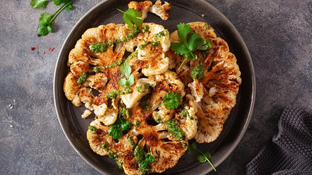 Geröstete blumenkohlscheiben im backofen, beträufelt mit grüner Soße und garniert mit Koriander.