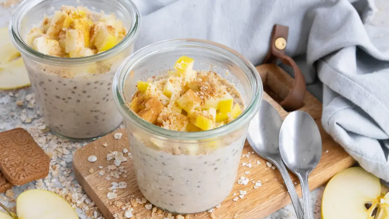 Zwei Gläser mit Overnight Oats Grundrezept, garniert mit Apfelstücken und Zimt. Perfekt für ein schnelles Frühstück.