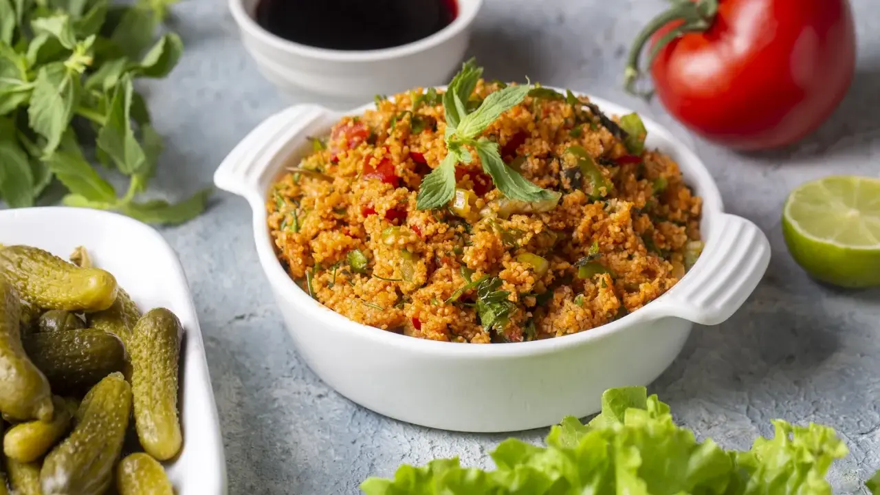 Ein köstliches Kisir-Rezept mit Bulgur, Tomaten und Kräutern, garniert mit Minze. Daneben Cornichons, Granatapfelsirup, Limette und ein frischer Kopfsalat.