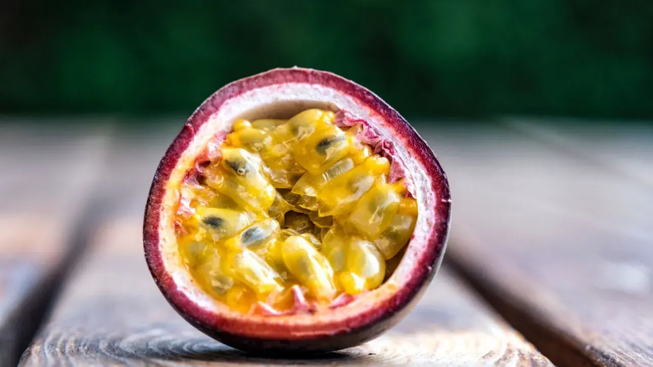 Eine aufgeschnittene Passionsfrucht mit saftigem, gelbem Fruchtfleisch und schwarzen Kernen liegt auf Holzplanken. Ein Genuss, diese Passionsfrucht zu essen!