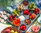 Leckere Picknick-Snacks: Erdbeeren, Gurken, Karotten, Nüsse, Tomaten, Pfirsiche und Brotscheiben mit Frischkäse auf einer Decke.
