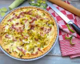 Herzhafte Quiche mit Lauch und Speck, perfekt für herzhafte Quiche Rezepte. Daneben liegen Lauch, ein Messer und ein Nudelholz.