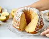 Saftiger Apfelkuchen mit Puderzucker, daneben ein Glas Apfelmus und frische Äpfel.