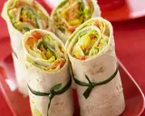 Vier gesunde wraps gefüllt mit knackigem Salat, Paprika und Karotten, kunstvoll mit grünen Bändern zusammengebunden.