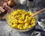 Schüssel mit warmem Kartoffelsalat, garniert mit Speck und Zwiebeln, bereit zum Servieren.