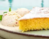 Ein Stück mallorquinischer Mandelkuchen mit zwei Kugeln Eis und Minze, serviert auf einem Teller am Pool.