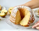 Ein saftiger Kuchen mit Apfelmus, bestäubt mit Puderzucker. Daneben liegen Äpfel und ein Glas Apfelmus.