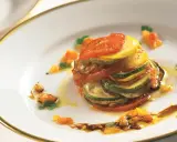 Ein kunstvoll geschichtetes Ratatouille-Rezept, inspiriert vom Film, mit Tomaten, Zucchini und Aubergine auf einem Teller mit goldenem Rand.