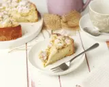 Ein Stück Streuselkuchen mit Pudding auf einem Teller, daneben eine Kaffeetasse und ein ganzer Kuchen.